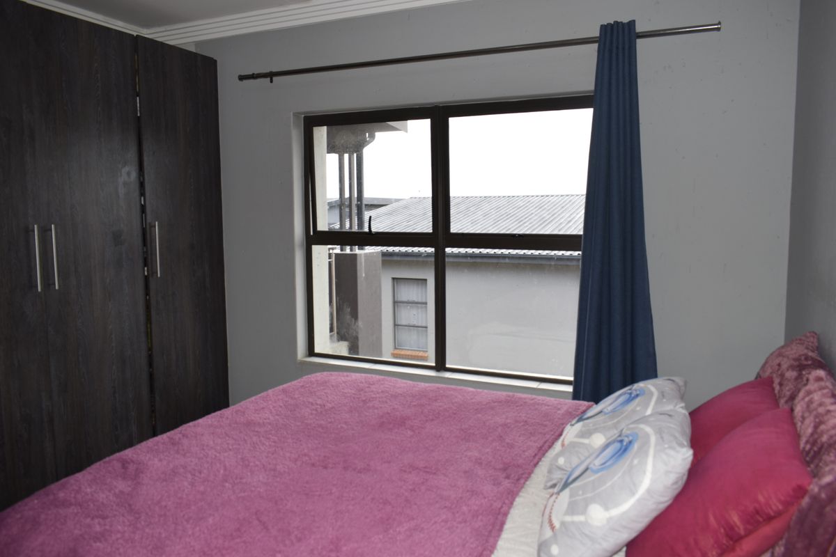 A bedroom featuring a built-in wardrobe and an aluminium-framed window, providing natural light and views of the surrounding townhouse complex.