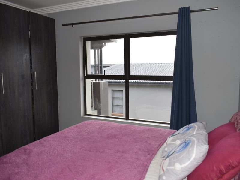 A bedroom featuring a built-in wardrobe and an aluminium-framed window, providing natural light and views of the surrounding townhouse complex.