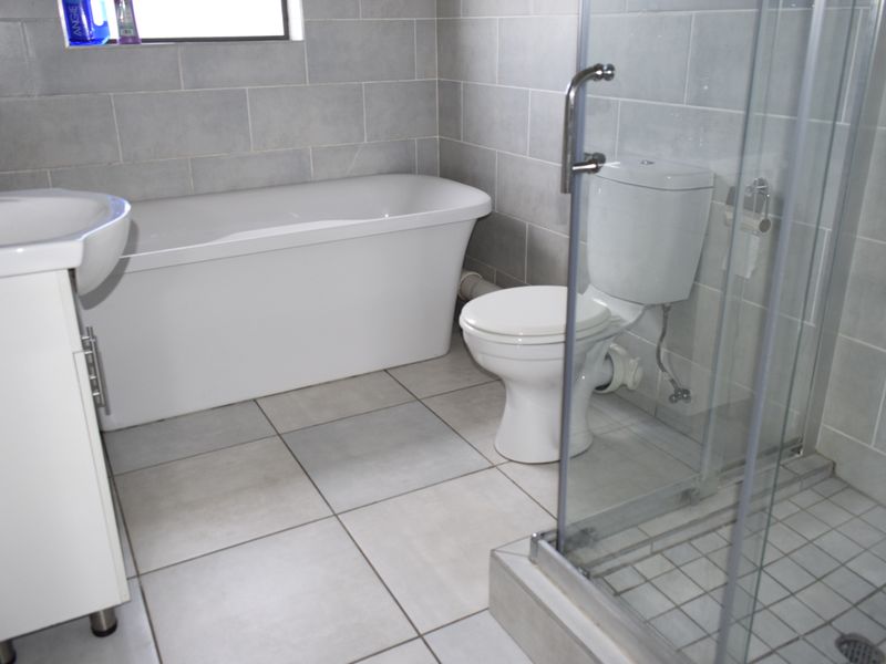 Modern bathroom featuring a freestanding bathtub, glass-enclosed shower, toilet, and vanity basin with neutral wall and floor tiling.