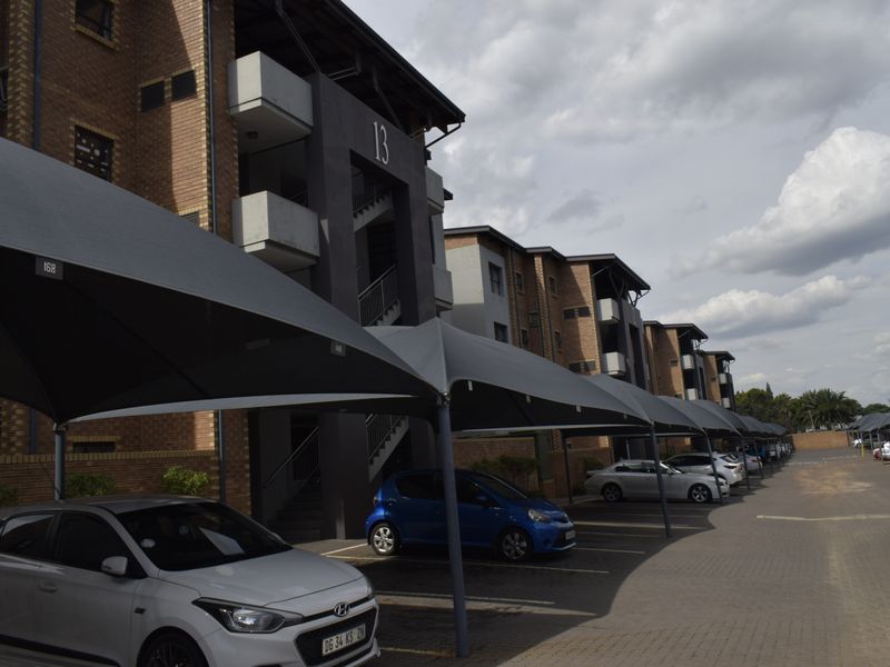 Exterior view of a townhouse complex featuring brick facade buildings and covered parking bays with shade cloth structures.