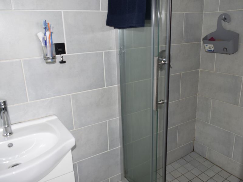 A functional bathroom featuring a modern vanity basin with mixer tap and a glass-enclosed shower with grey wall tiling.