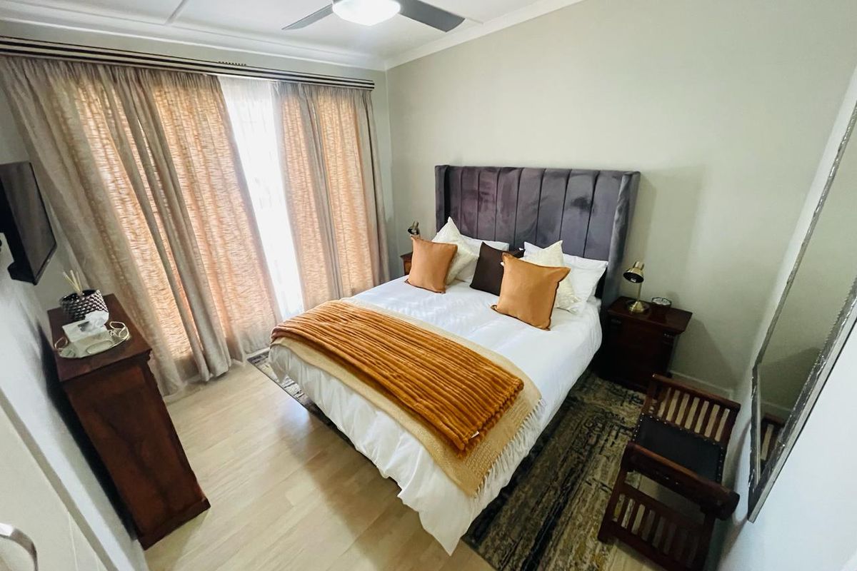 A well-maintained bedroom featuring light wood-look flooring, a ceiling fan, and large windows with curtains, providing a bright and comfortable living space.