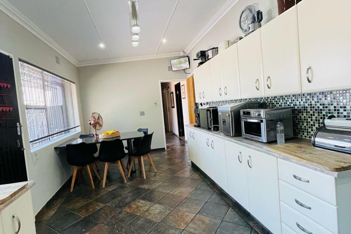 A functional kitchen featuring extensive white cabinetry, mosaic tile backsplash, and dark slate-style floor tiles with an integrated dining area.