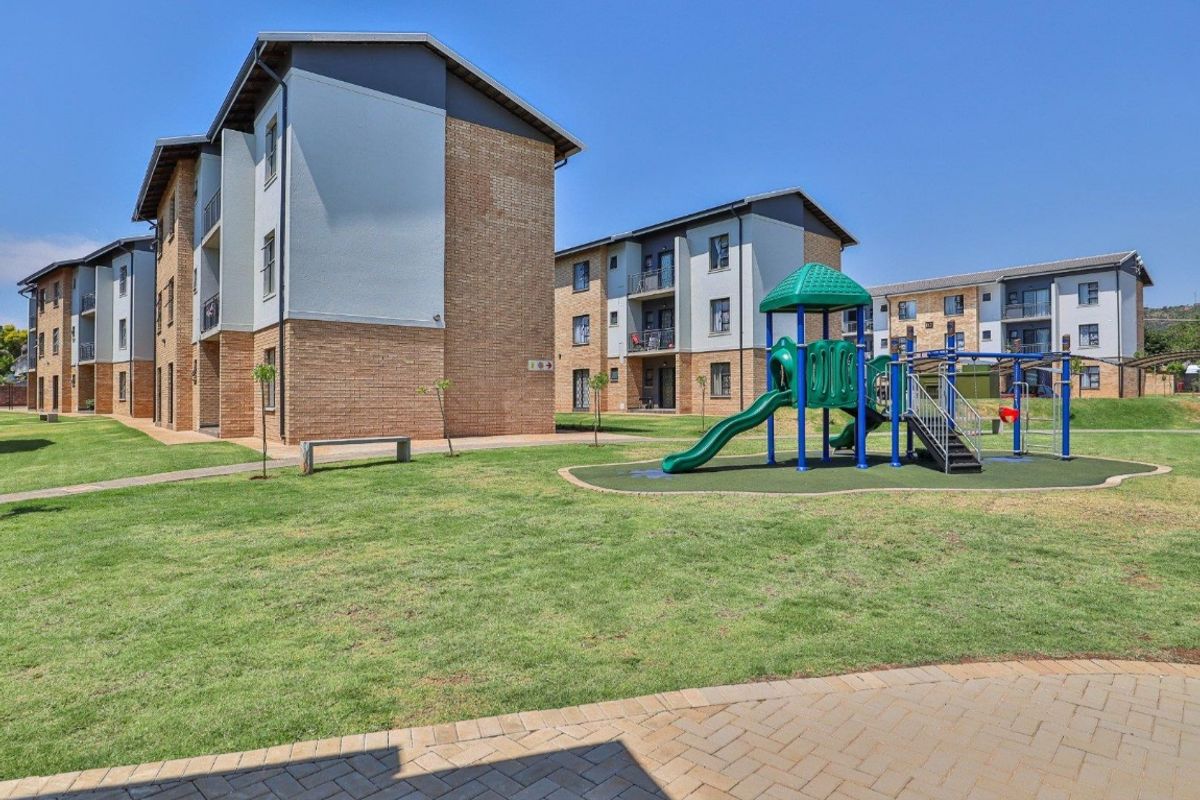 Exterior view of the apartment complex grounds featuring landscaped lawns, paved walkways, and a communal children's playground area.