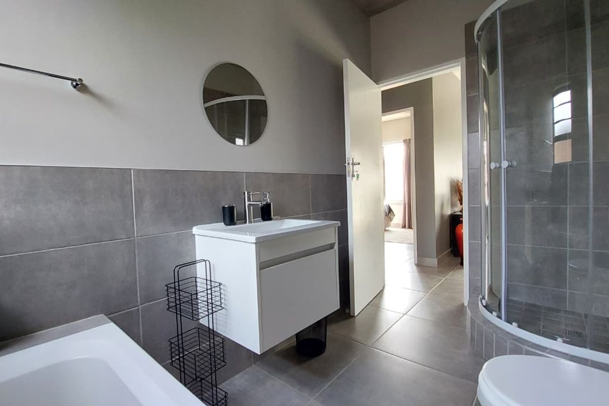 Modern bathroom featuring a glass-enclosed corner shower, a white vanity with a basin, and neutral grey wall and floor tiling.