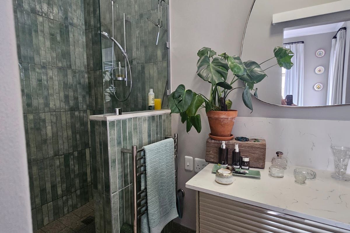 Modern bathroom featuring a walk-in shower with green vertical tiling, a sleek vanity with stone countertop, and a heated towel rail.