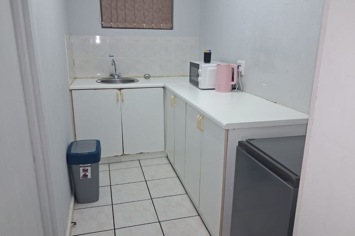 A compact kitchen area featuring white cabinetry, a stainless steel sink, tiled splashback, and tiled flooring.