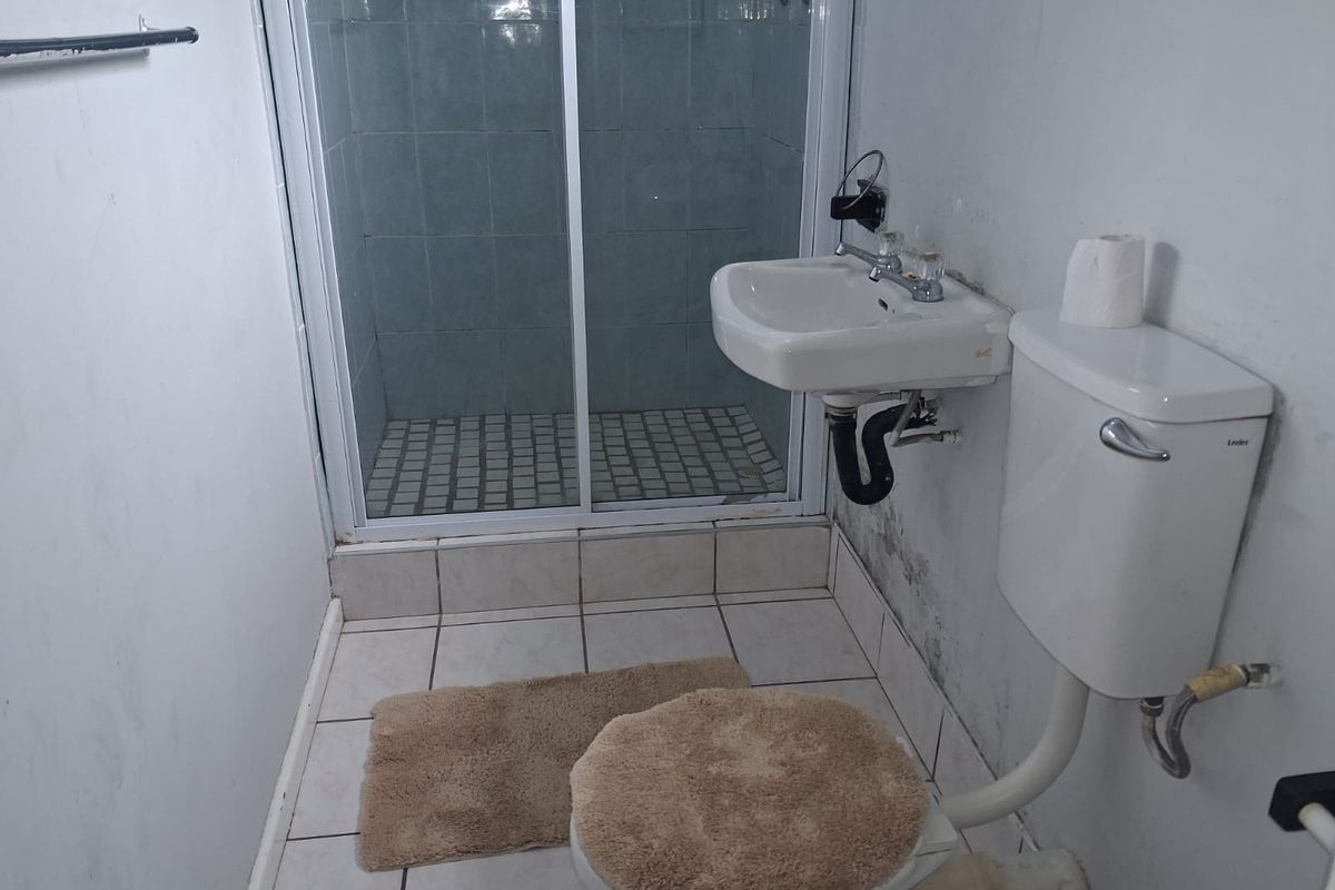 A compact bathroom featuring a shower enclosure, wall-mounted basin, and toilet, requiring cosmetic updates and maintenance to improve its overall condition.