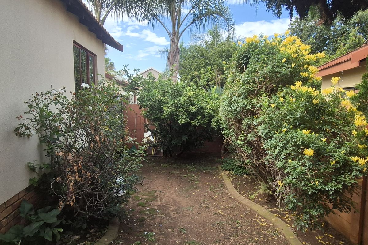 A private rear garden area featuring established shrubs, flowering plants, and a paved border along the side of the property.