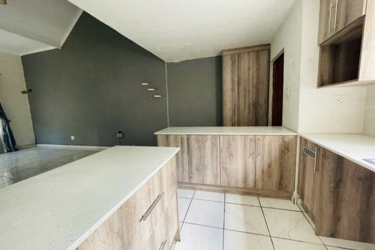 A modern kitchen featuring wood-finish cabinetry, stone countertops, and tiled flooring, set within an open-plan space with a vaulted ceiling.