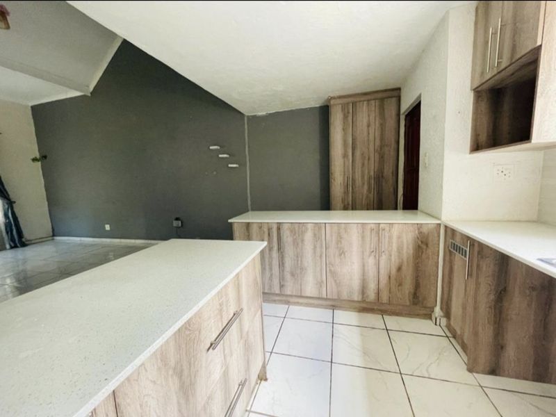 A modern kitchen featuring wood-finish cabinetry, stone countertops, and tiled flooring, set within an open-plan space with a vaulted ceiling.