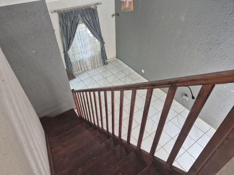 A view looking down a wooden staircase into an empty tiled living area with textured grey walls and natural light.