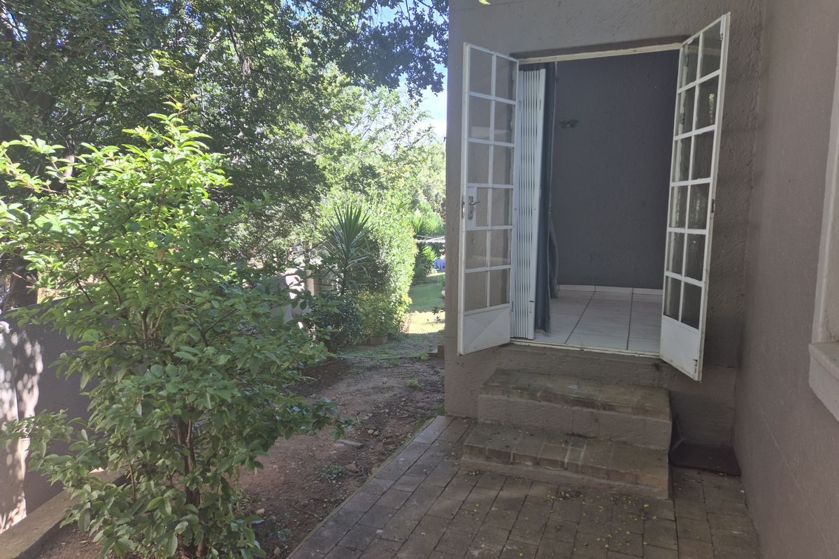 Rear exterior view of the townhouse featuring a paved patio area, concrete steps, and French doors leading into the interior living space.