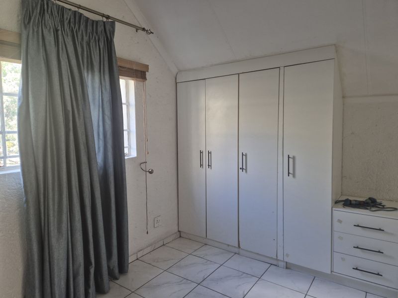 A bedroom featuring built-in cupboards, tiled flooring, and a sloped ceiling, offering functional storage space.