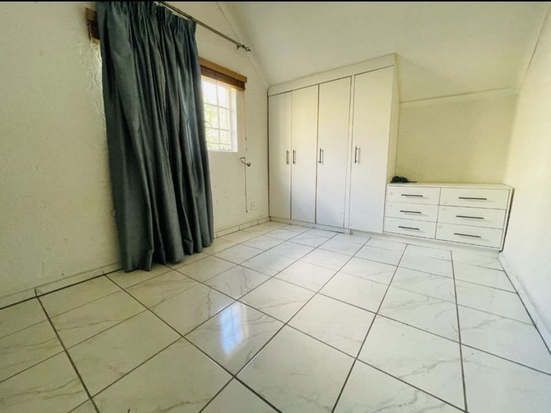 A bedroom featuring tiled flooring, sloped ceilings, and built-in cupboards, offering a functional space with potential for cosmetic updates.