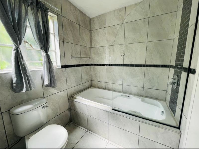 A functional bathroom featuring a built-in bathtub with a glass shower screen, tiled walls, and a standard toilet.