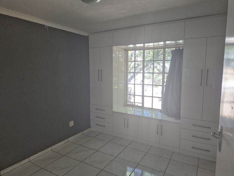 A bright bedroom featuring extensive built-in white cabinetry, a window seat, and tiled flooring, offering a clean and functional space.