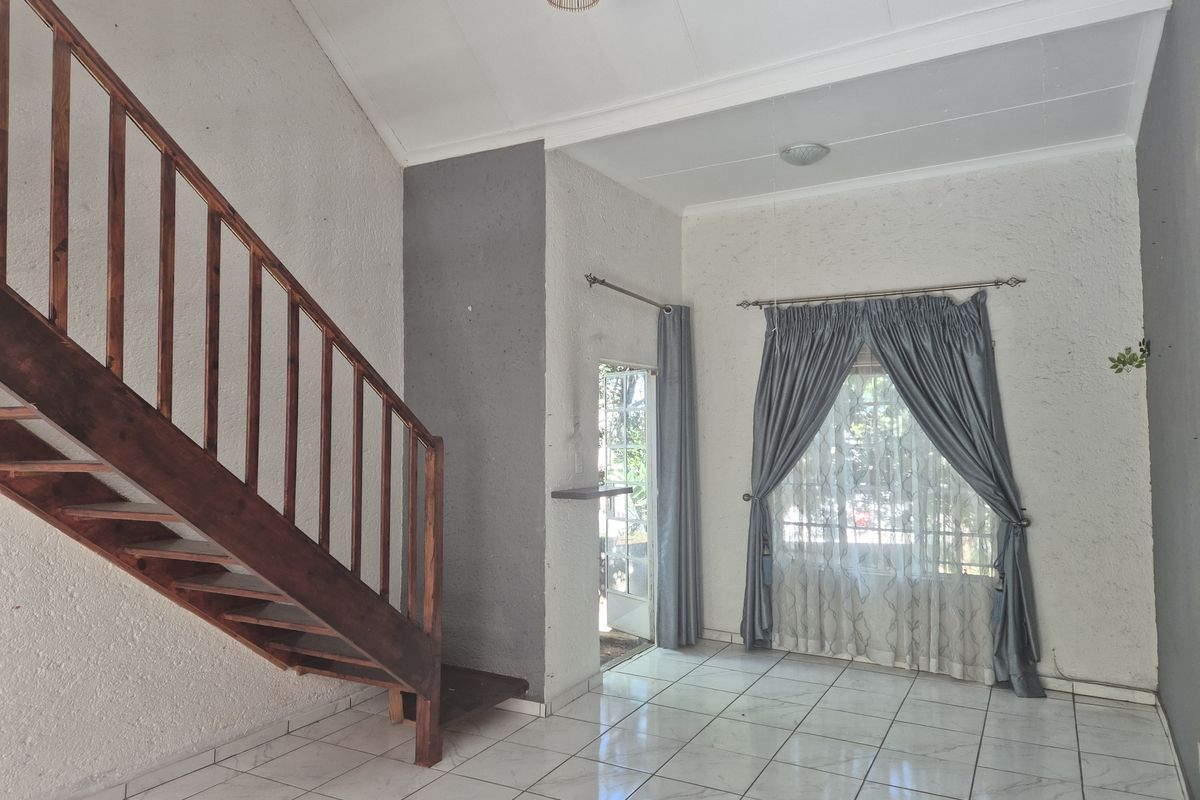 An open-plan living area featuring a prominent wooden staircase, tiled flooring, and textured walls, offering a blank canvas for interior design.