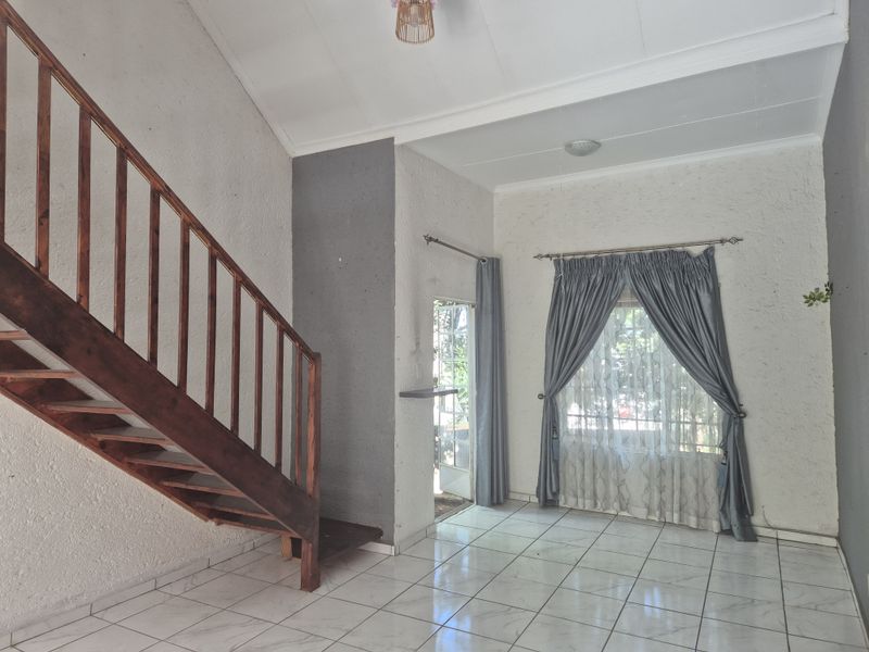 An open-plan living area featuring a prominent wooden staircase, tiled flooring, and textured walls, offering a blank canvas for interior design.