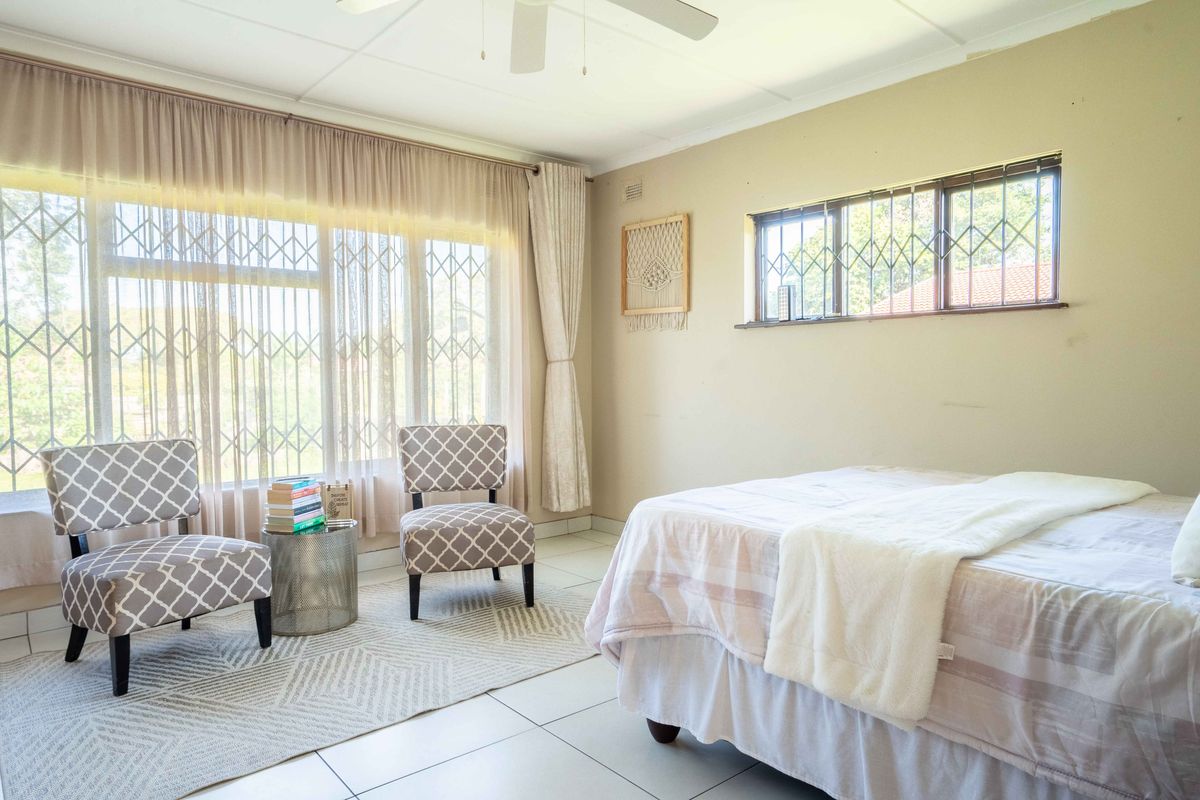 A bright bedroom featuring tiled flooring, a ceiling fan, and large windows fitted with security gates, offering a comfortable and functional living space.