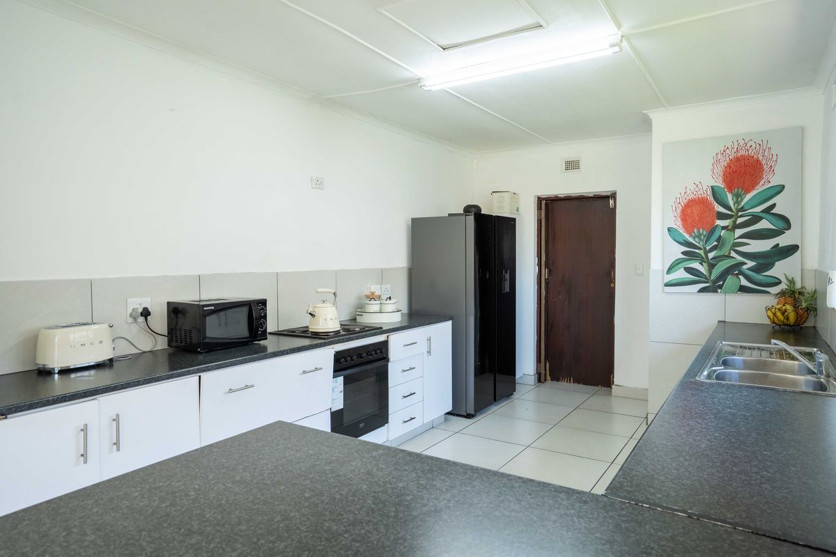 Functional kitchen featuring white cabinetry, dark laminate countertops, built-in oven, hob, and double bowl sink with tiled flooring.