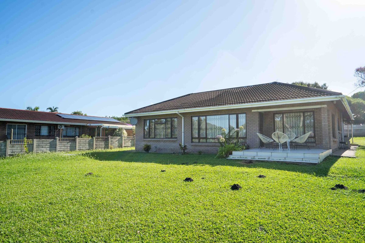 Rear view of a brick house featuring a tiled roof, security bars on windows, and a paved patio area overlooking a spacious lawn.