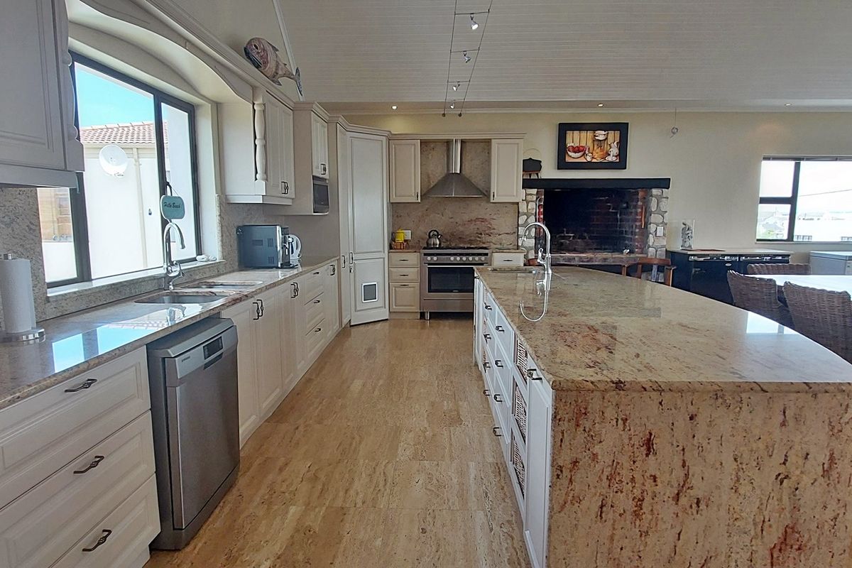 Spacious kitchen featuring granite countertops, a large central island, stainless steel appliances, and a unique brick fireplace, set against elegant travertine flooring.