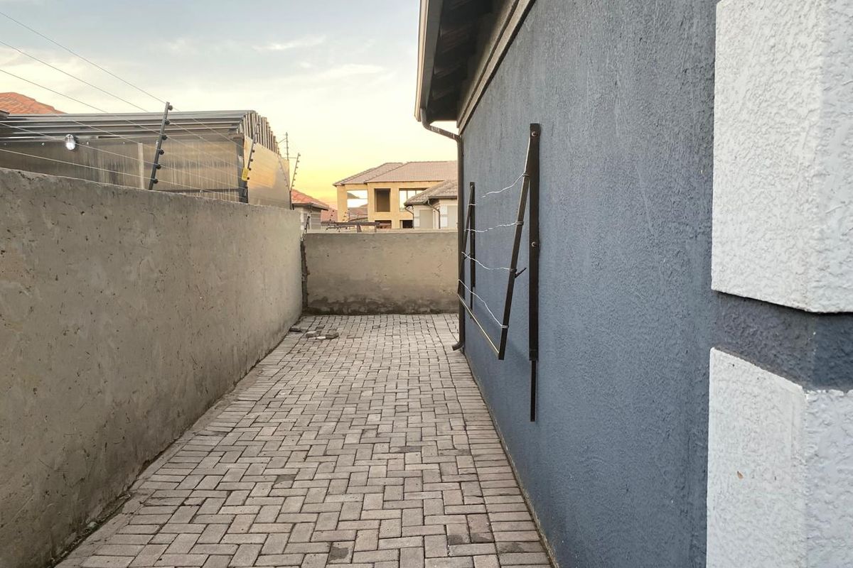 A side exterior walkway featuring paved flooring, a boundary wall with electric fencing, and a wall-mounted clothesline.