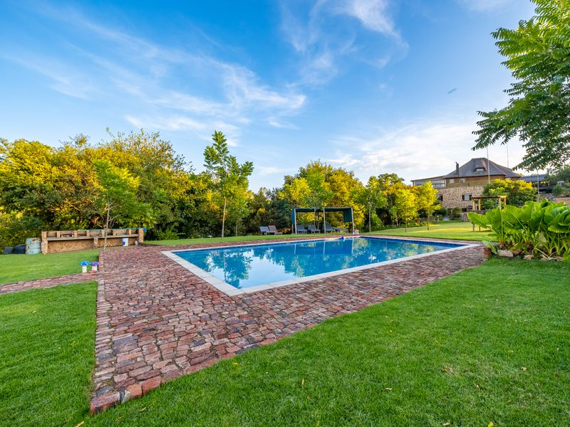 A well-maintained outdoor pool area featuring brick paving, a built-in braai, and lush garden surroundings, perfect for relaxation and entertainment.