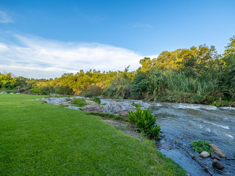 A scenic view of a flowing river bordered by a well-maintained green lawn and natural vegetation.
