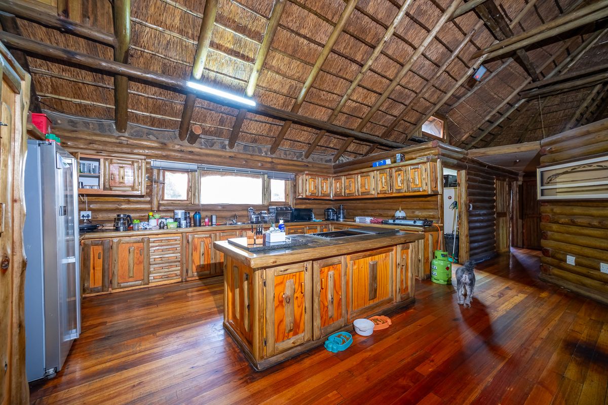 Rustic kitchen featuring custom wooden cabinetry, a central island with a built-in hob, and a traditional thatched roof with exposed timber beams.