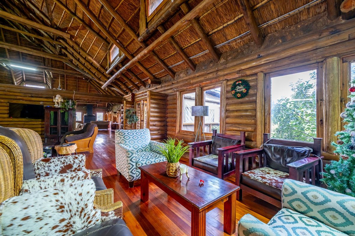 Spacious living area featuring authentic exposed log walls, high vaulted thatched ceilings, and warm hardwood flooring, creating a rustic and inviting atmosphere.