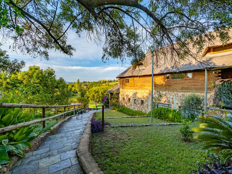 A scenic view of the rear exterior of a guest house featuring stone and timber construction, a thatched roof, and a stone-paved garden walkway.