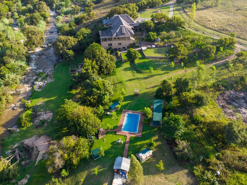 Aerial view of a sprawling guest house property featuring a swimming pool, extensive landscaped gardens, and direct river frontage in a scenic natural setting.