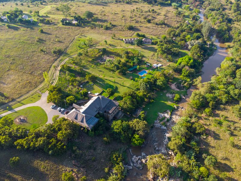 Aerial view of a sprawling guest house property featuring extensive grounds, a swimming pool, and scenic river frontage in a natural landscape setting.