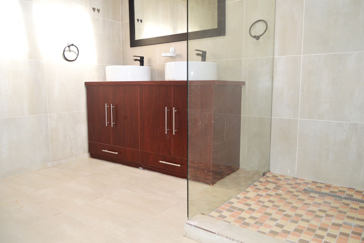 Modern bathroom featuring a double vanity with vessel sinks, a large wall mirror, and a walk-in shower with glass enclosure.