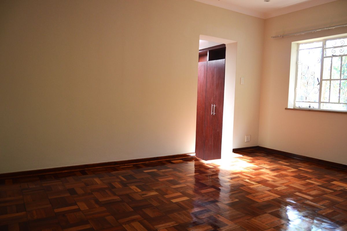 A bright bedroom featuring polished parquet timber flooring, neutral walls, and a built-in wooden wardrobe.