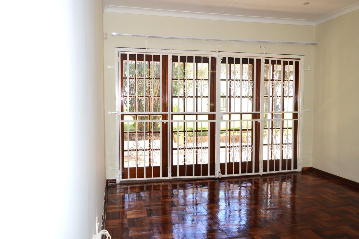 A bright living area featuring polished parquet flooring and large wooden French doors secured with white metal security gates.