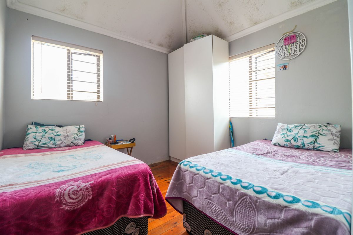 A bedroom featuring timber flooring, built-in wardrobe, and dual windows, currently showing signs of ceiling water damage requiring maintenance.