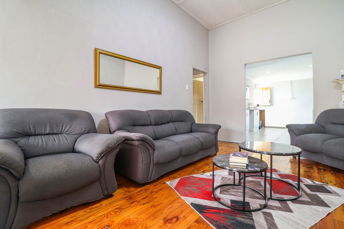 A living room featuring original hardwood flooring and a coved ceiling, with an open transition leading into the kitchen area.