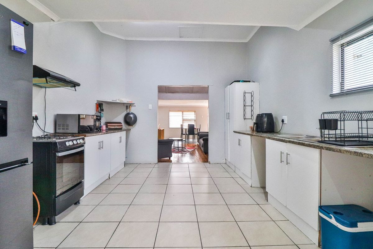 Functional kitchen featuring white cabinetry, granite countertops, tiled flooring, and an extractor fan, with an open-plan flow into the adjacent living area.