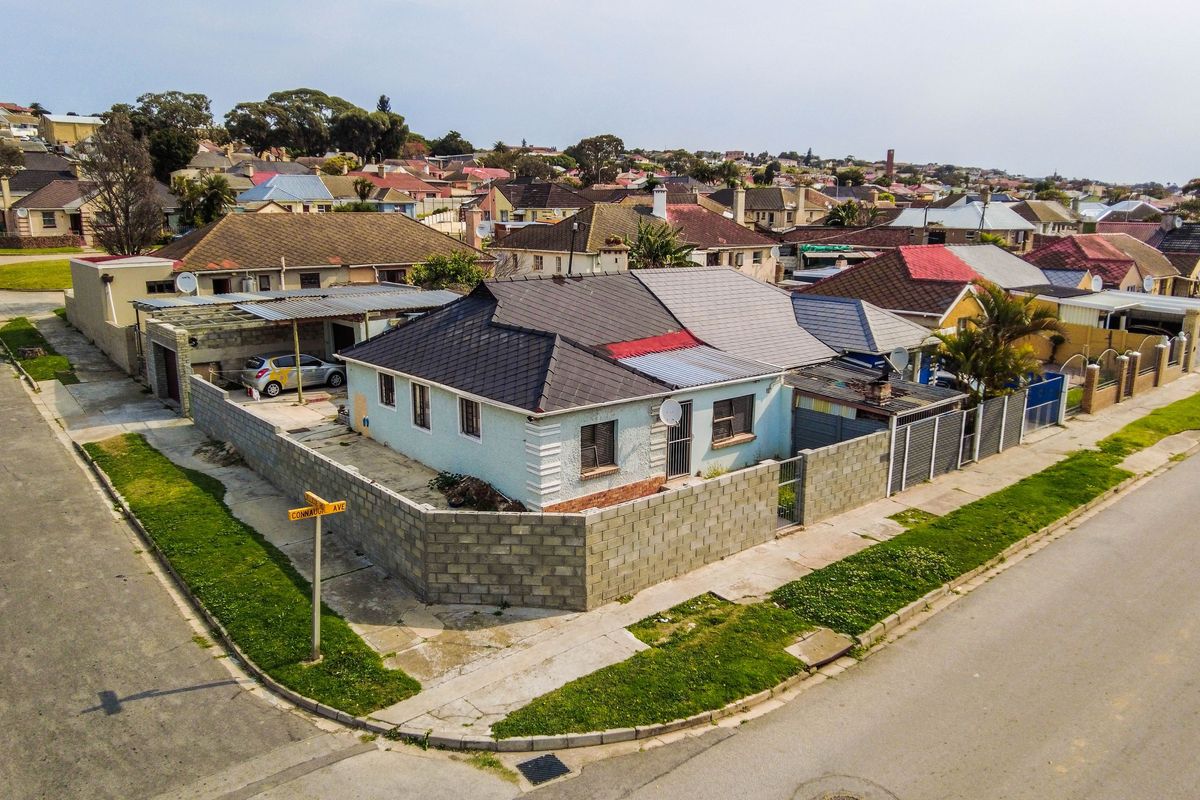 Aerial view of a corner property featuring a tiled roof house, concrete block boundary walls, and a carport in a residential neighbourhood.