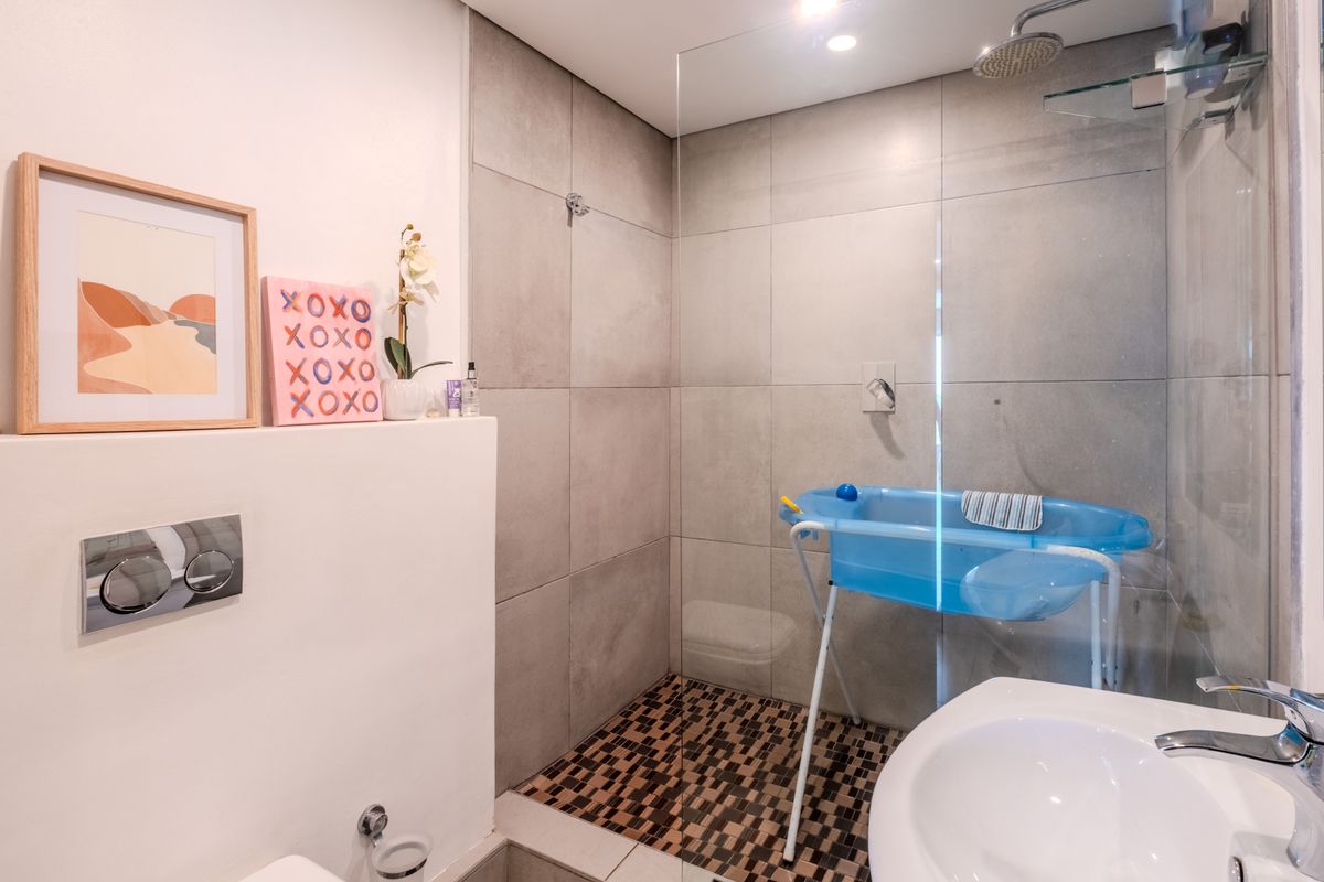 Modern bathroom featuring a walk-in shower with a glass screen, rain shower head, mosaic floor tiling, and a wall-mounted toilet flush system.