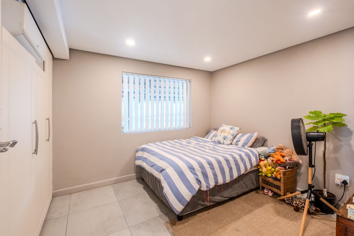 A well-maintained bedroom featuring tiled flooring, built-in wardrobe storage, a split-system air conditioner, and vertical blinds for privacy.