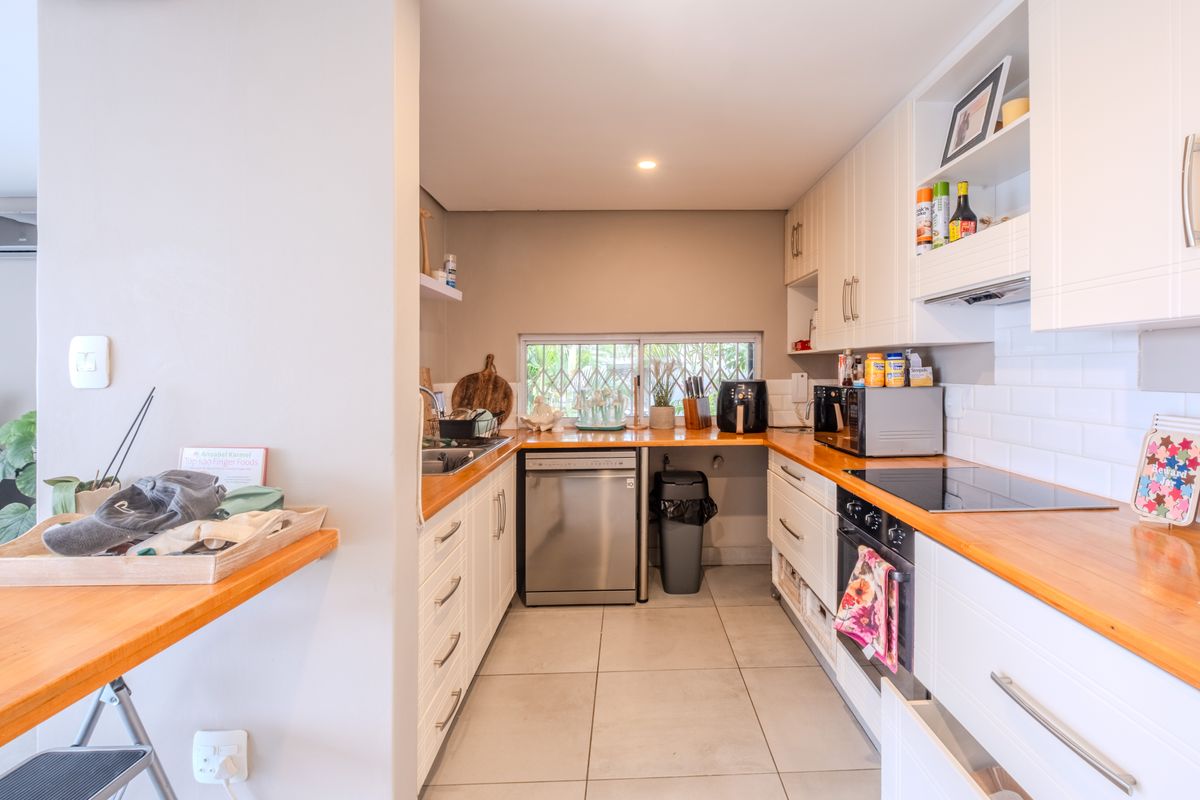 A functional kitchen featuring white cabinetry, warm wooden countertops, a subway tile backsplash, and integrated appliances including an oven and electric hob.