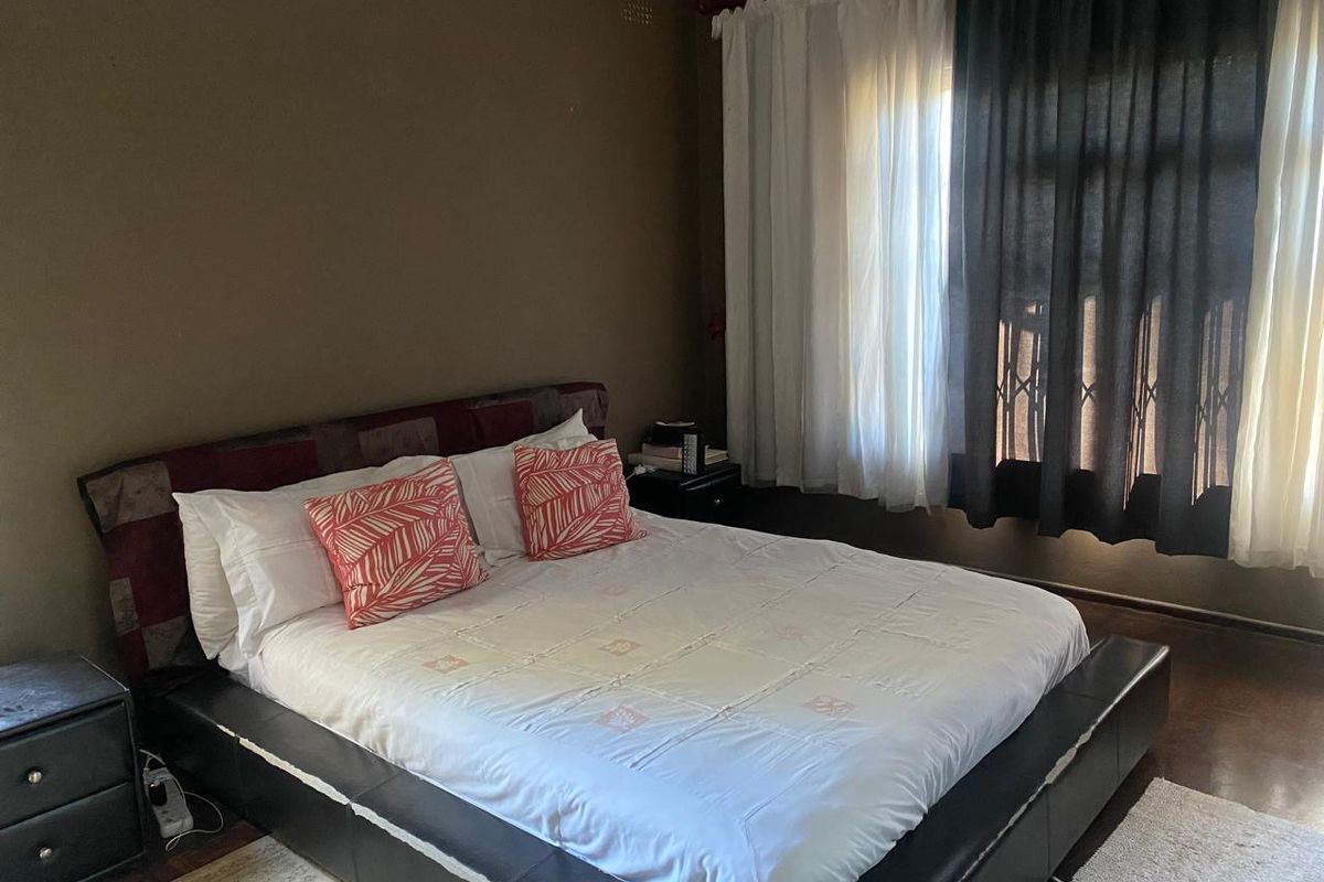 A bedroom featuring dark-toned walls, wooden flooring, and a window fitted with layered curtains and security gate.
