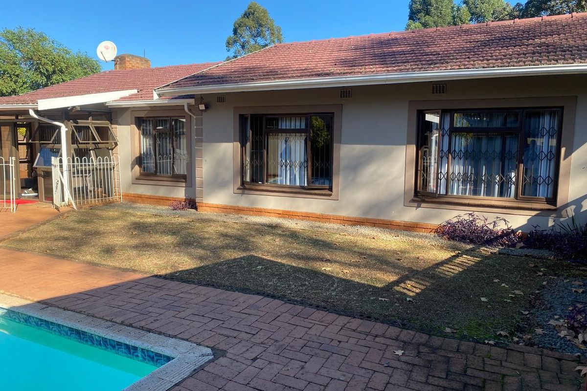 Rear view of the house featuring a tiled roof, brick-paved patio area, and a swimming pool set against a landscaped garden.