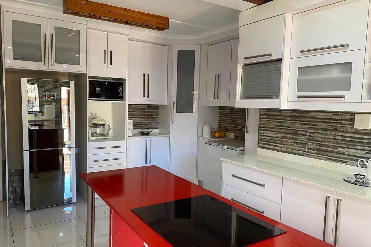 Modern kitchen featuring white cabinetry, a striking red island with an integrated induction hob, stone countertops, and decorative tiled backsplash.