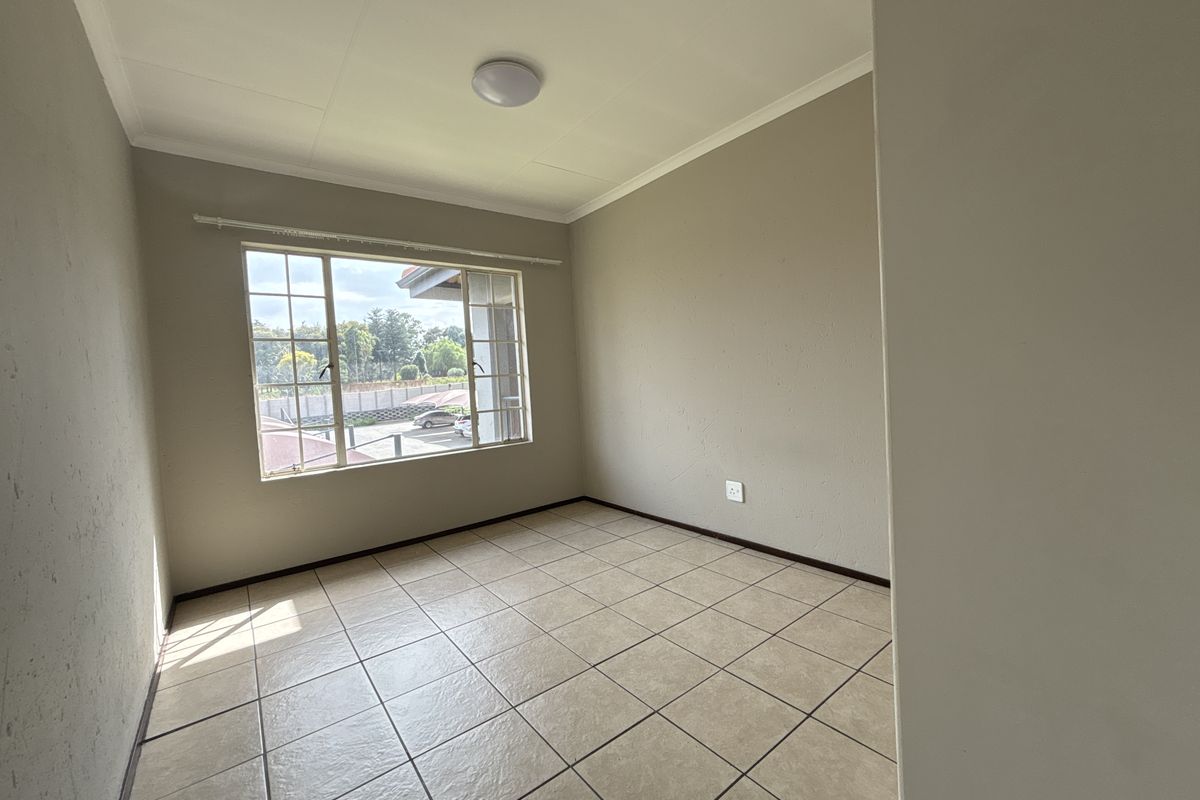 A bright, empty bedroom featuring neutral wall paint, tiled flooring, and a large window providing natural light.