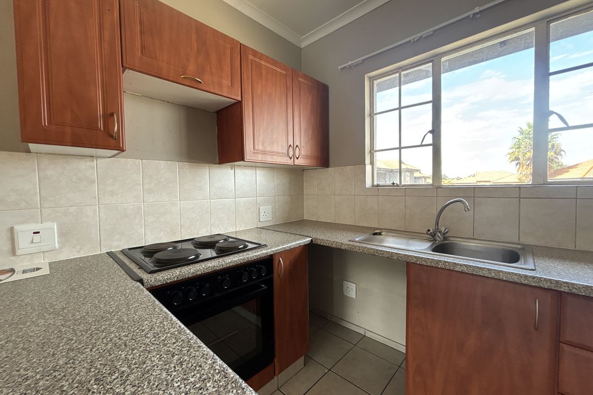 A functional kitchen featuring laminate cabinetry, built-in electric oven and hob, stainless steel sink, and tiled splashbacks with natural light.